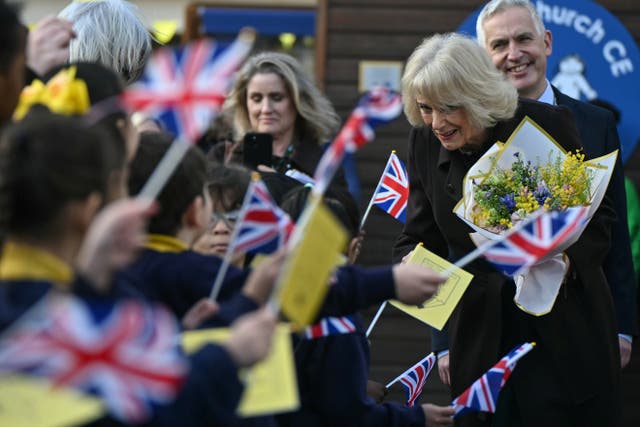 Camilla holding a bunch of flowers while saying goodbye to children waving mini Union flags