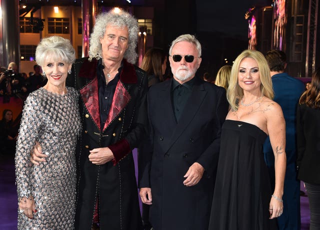 Roger Taylor and Brian May with their wives, posing for the cameras