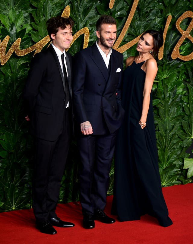 Brooklyn Peltz Beckham, Sir David Beckham and Victoria Beckham posing for a photo at a red carpet event, with Victoria looking across at her son