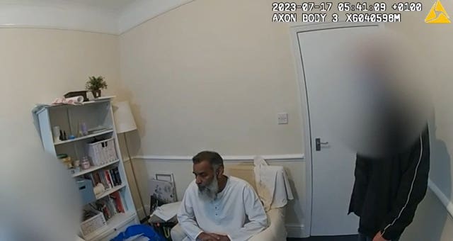 Anjem Choudary sits in a chair as he is arrested by Metropolitan Police officers