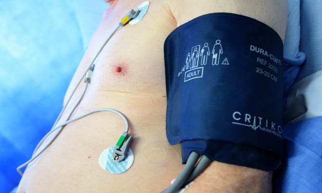 A patient sits in a hospital bed with a blood pressure cuff attached to his arm