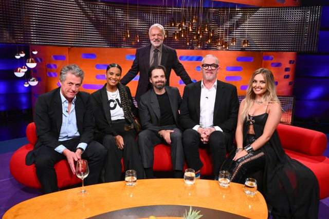 Hugh Grant, Neneh Cherry, Sebastian Stan, Greg Davies, Perrie Edwards sitting on a sofa, with Graham Norton standing behind them