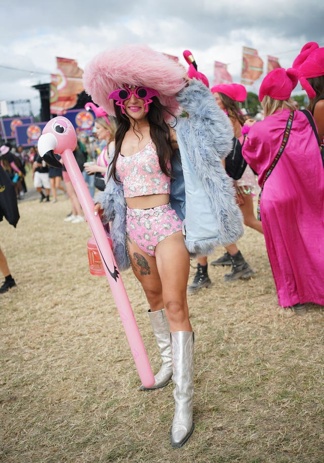 A woman dressed in a fluffy hat and coat, hot pants and vest, silver boots, carrying a blow-up flamingo