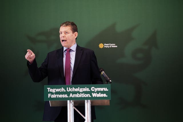 Plaid Cymru leader Rhun ap Iorwerth stands in front of a dragon image as he gestures at the launch of his party's manifesto