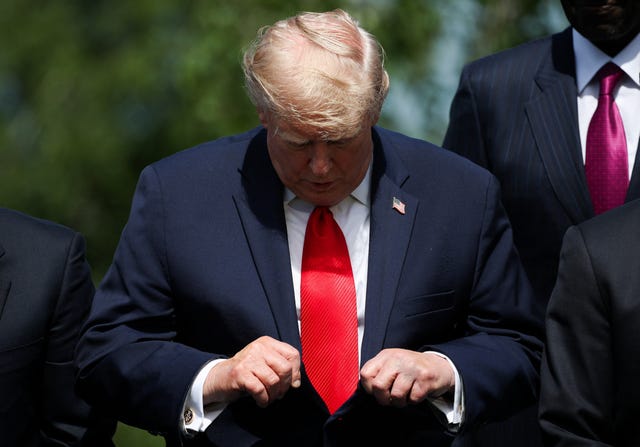 US President Donald Trump checks his tie as he waits for a family photo during the G7 summit in Evian