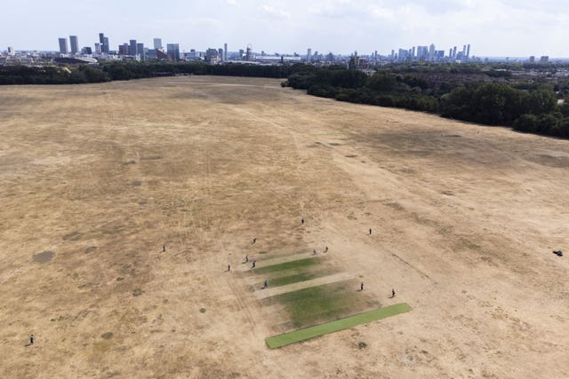 Cricketers play on small patches of green grass surrounded by scorched earth at Hackney Marshes, east London 