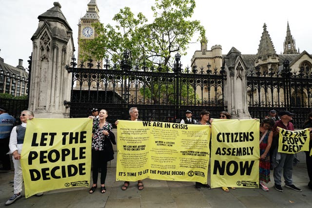 Members of Extinction Rebellion protest outside Parliament holding a number of yellow banners saying "Let the people decide" and "Citizens assembly now".