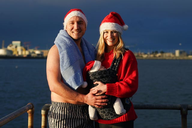 A couple and a baby all wearing Father Christmas hats