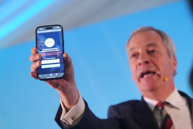 Reform UK leader Nigel Farage holding a phone displaying the number of Reform UK party members whilst speaking during the Reform UK East of England conference at Chelmsford City Racecourse