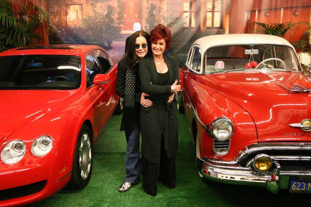 Ozzy and Sharon Osbourne pose in front of two cars