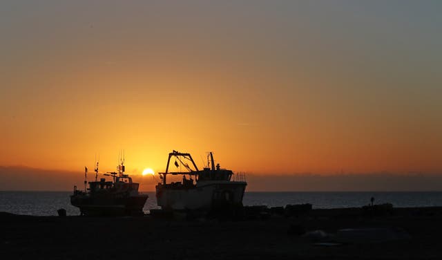 The sun rises behind fishing boats on the beach in Dungeness, Kent