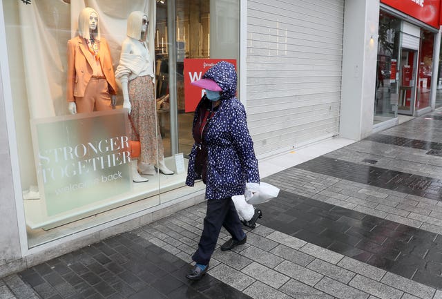 A woman wearing a face covering passes a shop window in Belfast