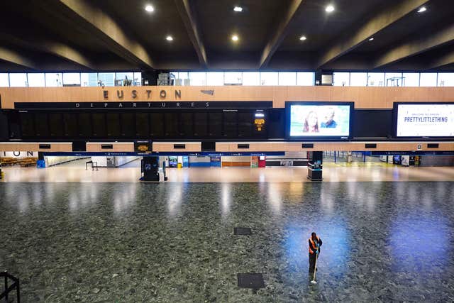 A person sweeping the floor in front of an empty departures board at Euston station in London 