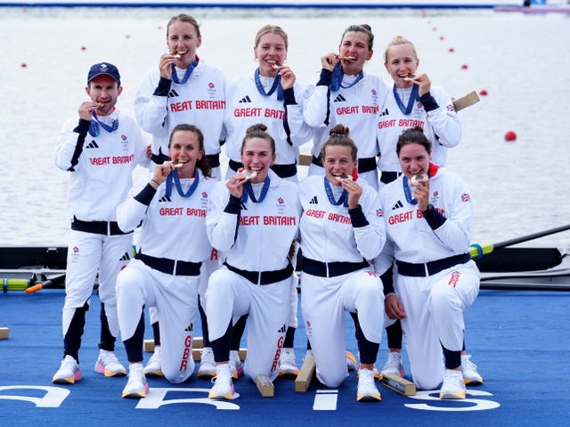 Team GB coxswain Henry Fieldman on the left and the women's eight celebrate their bronze by biting their medals at the Paris Olympics