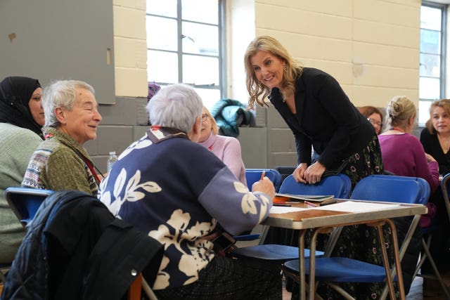 Sophie leans on a chair as she chats to women sat at a table