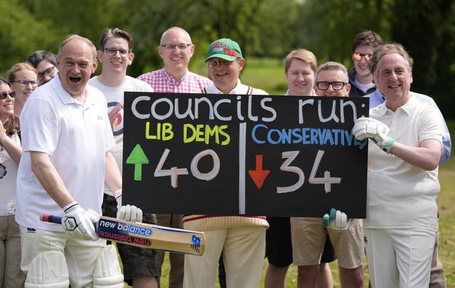 Sir Ed Davey, wearing cricket whites, celebrates next to a board showing an increase in the number of councils run by the Lib Dems and a fall in the number run by the Conservatives