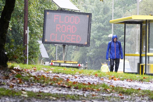 A man in a blue coat walks past a flood sign in Liverpool