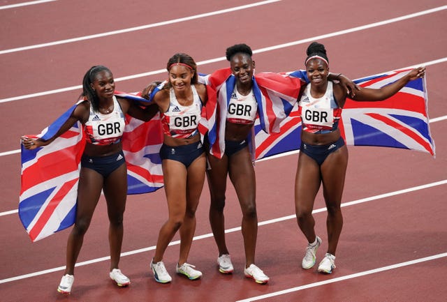 Team GB's Tokyo 2020 Olympic bronze medal-winning women's relay team stand on a track draped in Union Jack flags 