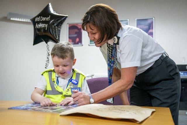 Boy and police officer at a table with a black balloon behind them with the words Well Done Anthony on it