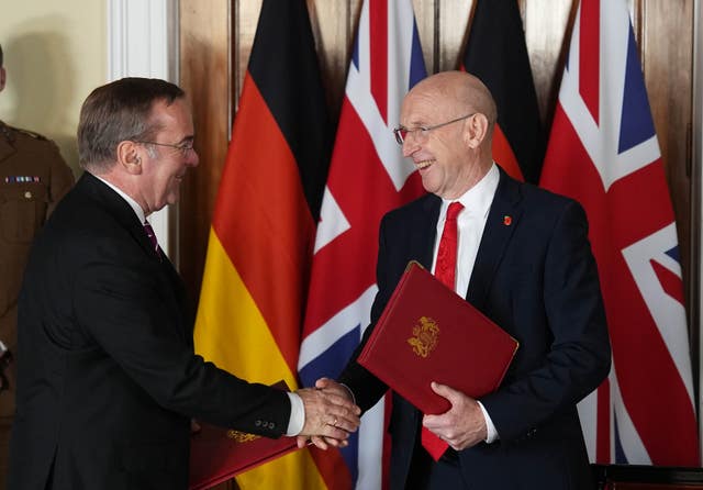 John Healey shakes hands with Boris Pistorius in front of UK and German flags