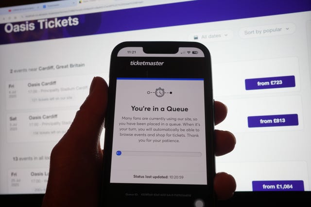Phone showing 'you are in the queue' in front of a laptop displaying concert dates