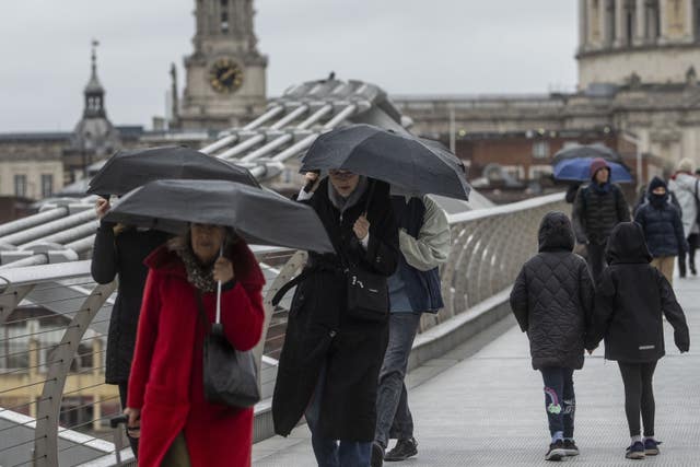 People with umbrellas cross the Millennium Bridge in London