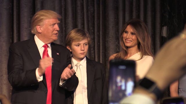 Donald Trump clapping while standing next to his son Barron and wife Melania