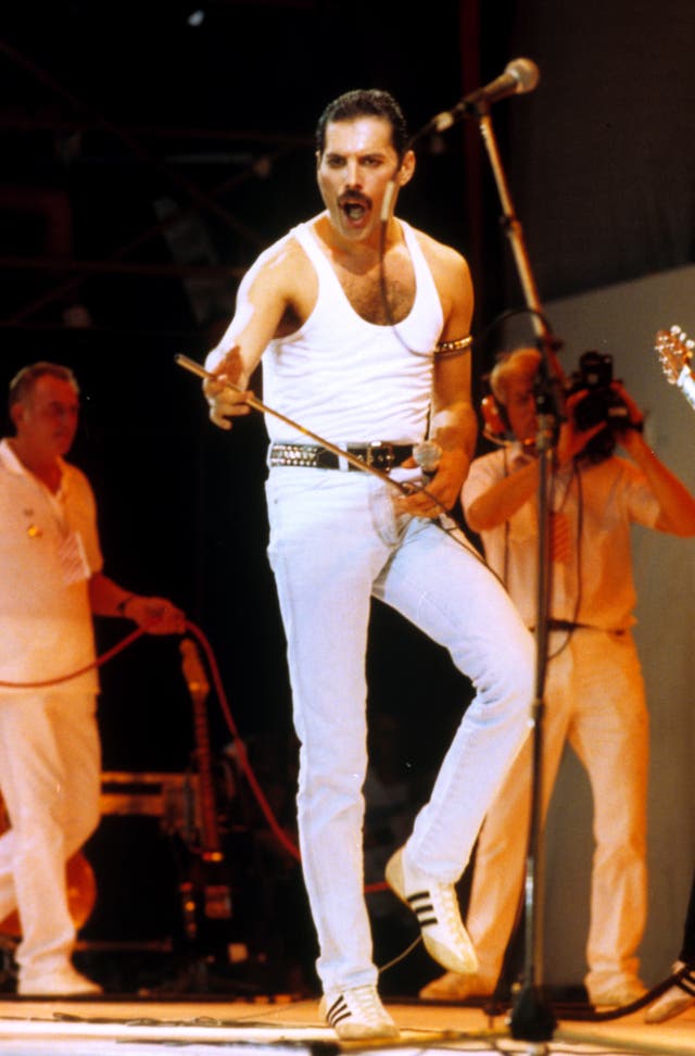 Freddie Mercury wearing a white tank and jeans holding a microphone on stage at Live Aid