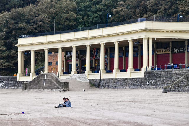People sit on an almost deserted beach at Barry Island in the Vale of Glamorgan (Ben Birchall/PA)