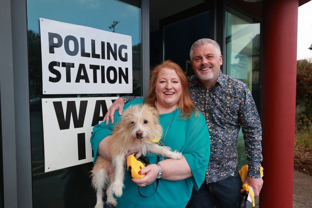 Naomi Long smiling while holding her dog in her arms, while her husband Michael has his arm round her shoulder