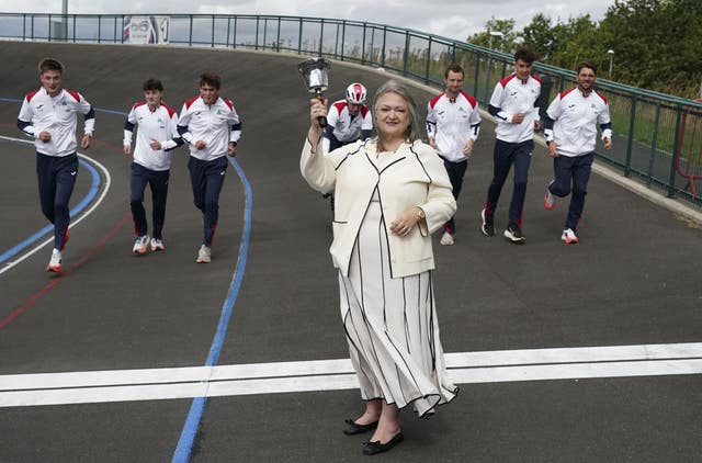Frances Connolly ringing a bell while standing at the finish line of a track at Middlesbrough Velodrome as men in tracksuits run towards her