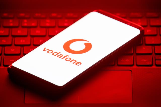 Smartphone shows the Vodafone logo displayed as it rests on a laptop keyboard illuminated red 