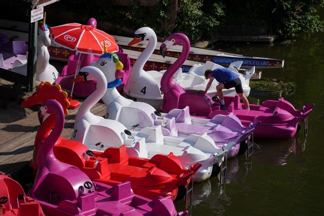 A man cleans pink and white pedalos on a river