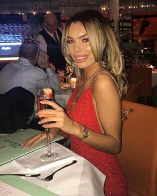 Handout photo of Ashley Dale smiling, seated at table holding a drink