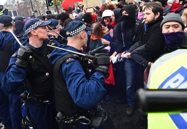 Police officers holding truncheons attempt to keep the crowds under control