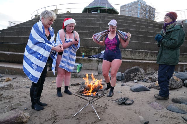 Swimmers dry off by a fire after taking a Christmas Day dip
