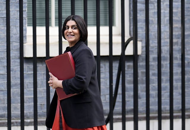 Shabana Mahmood smiling while walking along Downing Street, carrying a red ministerial folder