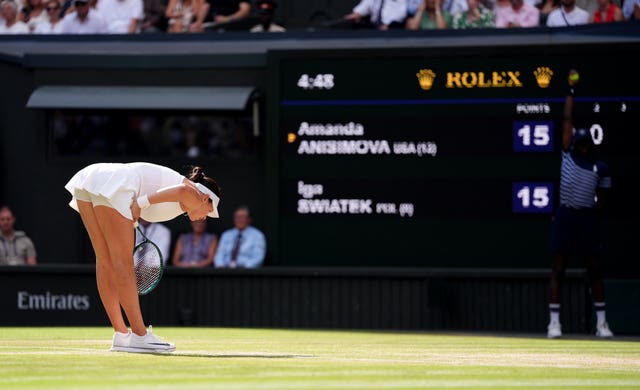 Amanda Anisimova crouches down in front of the scoreboard as she tries to compose herself