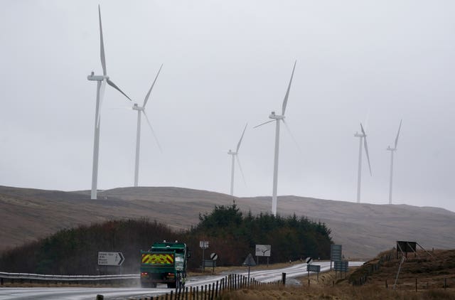 Wind turbines rise from the mist on hills near a road