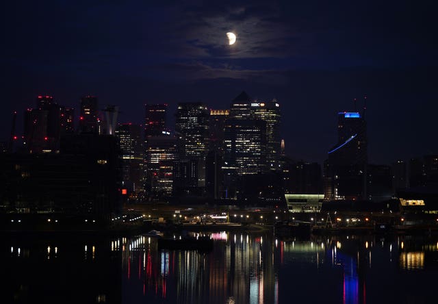 A lunar eclipse is visible above Canary Wharf in London as the full moon passes into Earth’s shadow