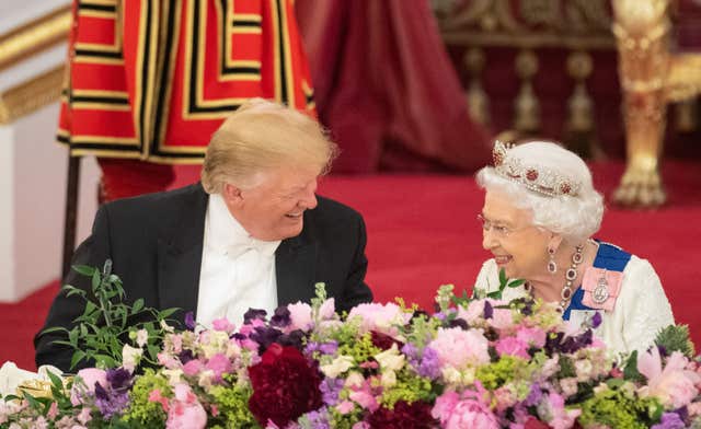 President Trump and the late Queen smile at one another as they sit at the state banquet table side by side 