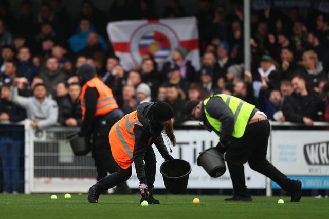 Stewards clear up fake money, tennis balls and flares thrown onto the pitch by Reading fans