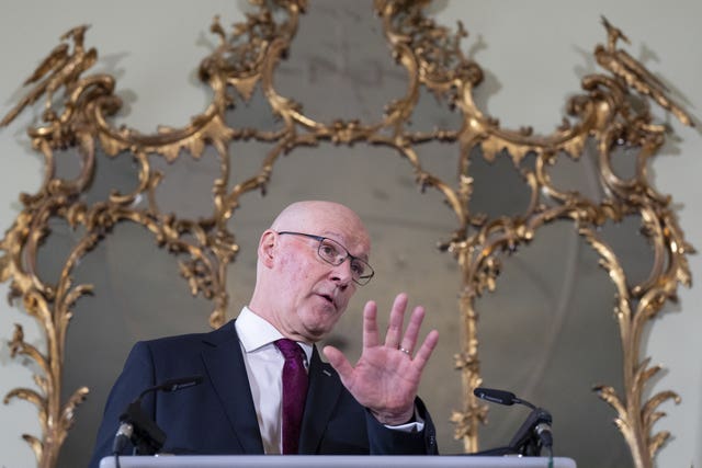 John Swinney speaking in front of a large, gold-framed mirror