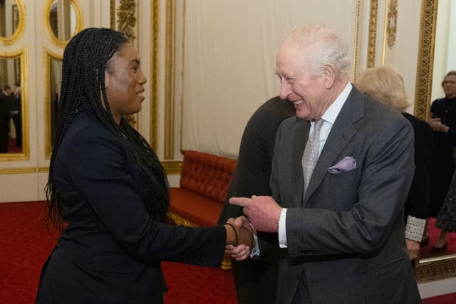 The King pointing with his left hand while using his right hand to shake hands with Kemi Badenoch as the pair smile at each other