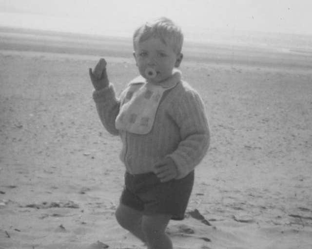 Alexander Blue as a child on a beach wearing a bib and with a dummy in his mouth
