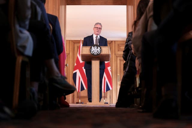 Sir Keir Starmer flanked by two Union flags while standing at a lectern at the front and centre of two rows of journalists in Downing Street