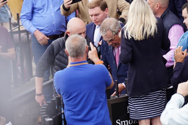 Nigel Farage is escorted back to his campaign bus after a milkshake was thrown at him in Clacton, surrounded by a crowd and the media