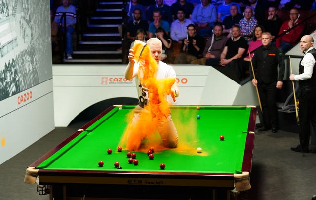 A 'Just Stop Oil' protester jumps on the table and throws orange powder during the match between Robert Milkins and Joe Perry 