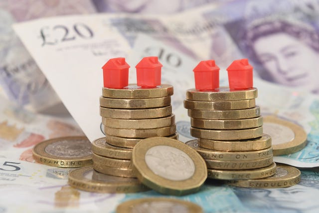 Small monopoly-like houses sit on top of two piles of coins and bank notes