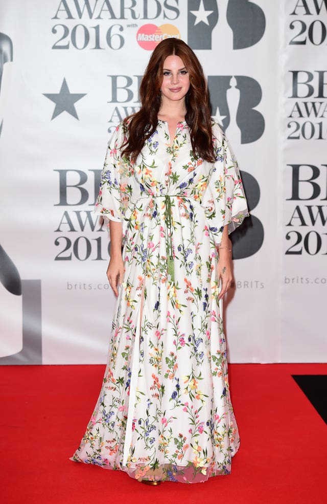 Lana Del Rey posing for photos at a red carpet event, wearing a floral gown